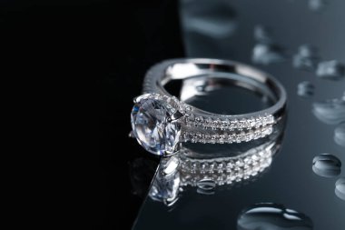 Luxury jewelry. Stylish presentation of elegant ring on mirror with water drops, closeup. Space for text