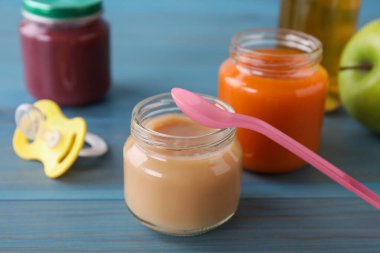 Jars with healthy baby food, bottle of juice, apple, spoon and pacifier on light blue wooden table