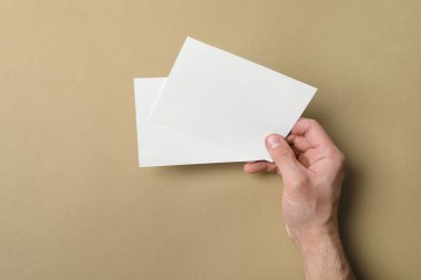 Man holding flyers on light brown background, closeup. Mockup for design