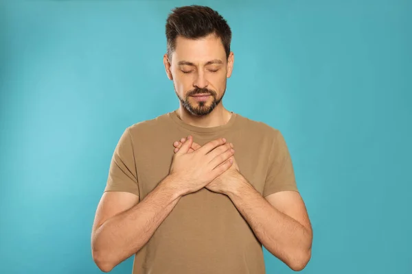 Man with clasped hands praying on turquoise background