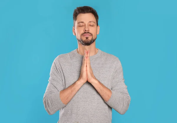 Man with clasped hands praying on turquoise background