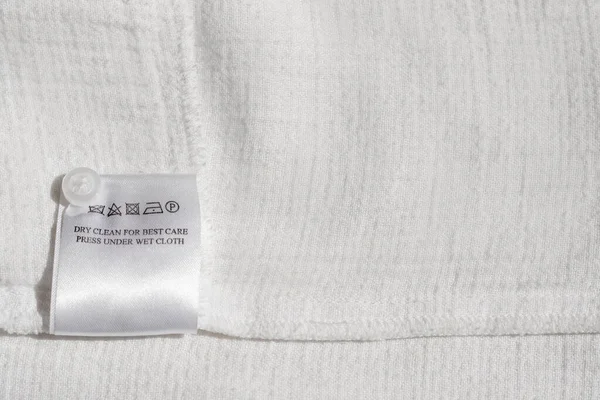 Clothing label with instruction on white garment, top view. Space for text