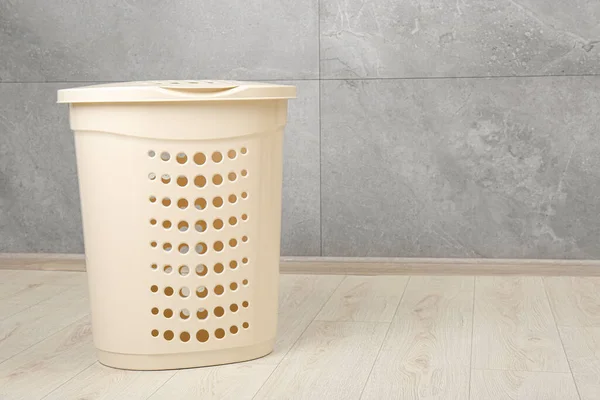 Empty plastic laundry basket near grey wall. Space for text