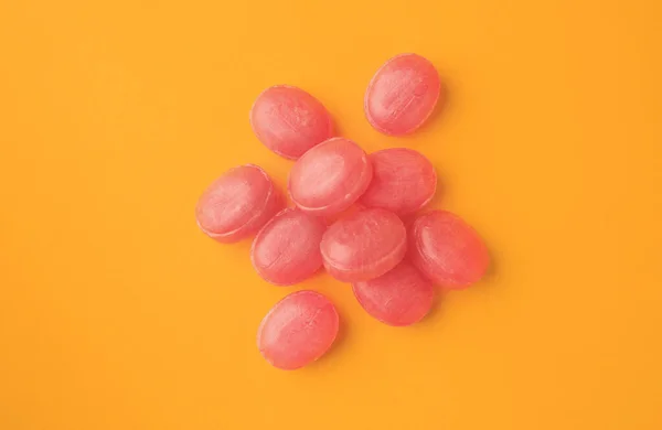 Many pink cough drops on orange background, flat lay