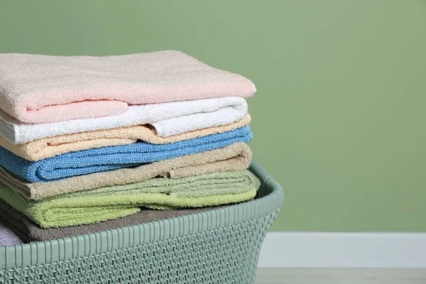 Plastic laundry basket with clean terry towels on floor near light green wall, closeup. Space for text