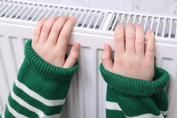 Girl warming hands on heating radiator, closeup
