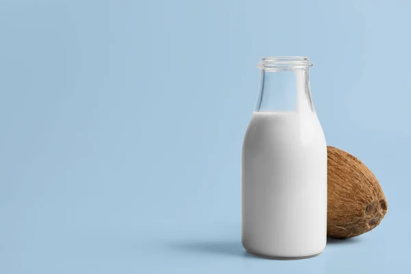 Glass bottle of delicious vegan milk and coconut on light blue background, space for text