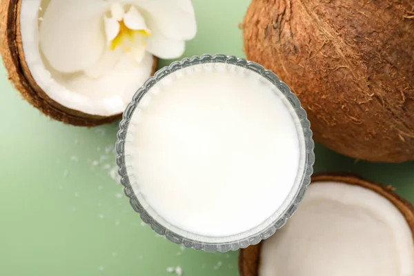 Glass of delicious vegan milk, coconuts and flower on green background, flat lay