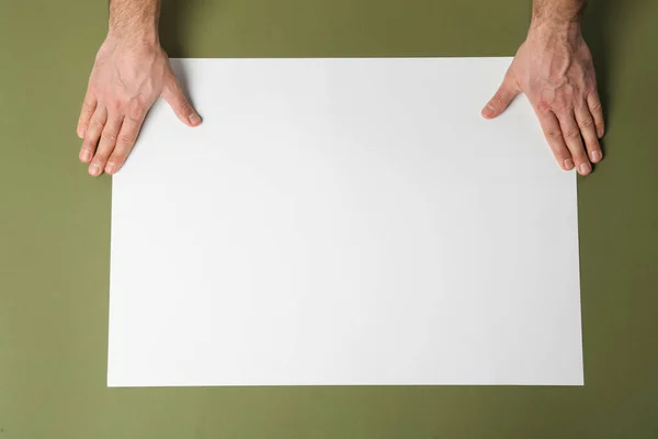 Man with empty sheet of paper on olive background, top view. Mockup for design