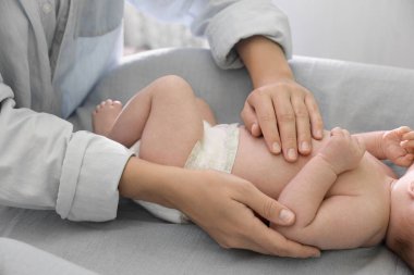 Mother taking care of her baby on changing table indoors, closeup