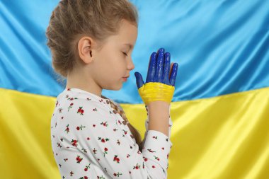 Little girl with clasped painted hands near Ukrainian flag