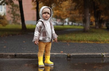 Cute little girl standing in puddle outdoors