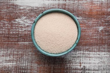 Bowl of active dry yeast on wooden table, top view