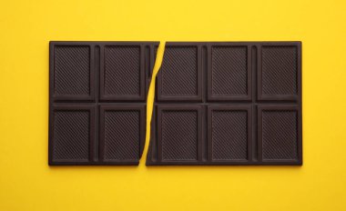 Broken chocolate bar on yellow background, top view