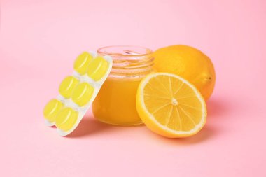 Blister with cough drops, fresh lemons and honey on pink background