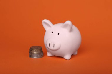 Ceramic piggy bank and coins on orange background. Financial savings
