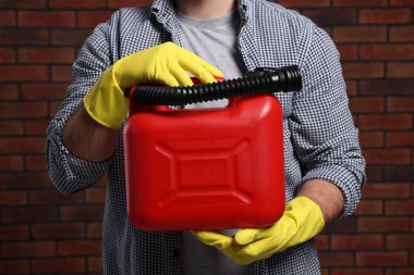 Man holding red canister against brick wall, closeup