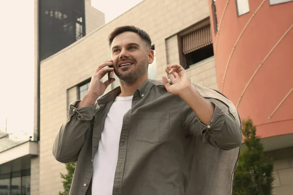 Man holding garment cover with clothes while talking on phone outdoors. Dry-cleaning service