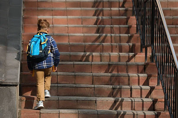Little boy with backpack going up stairs to school, back view