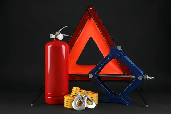 Emergency warning triangle, red fire extinguisher, towing strap and scissor jack on black background. Car safety