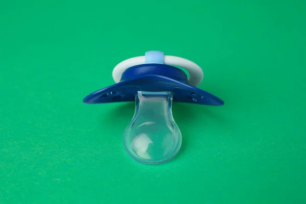 One blue baby pacifier on green background, closeup