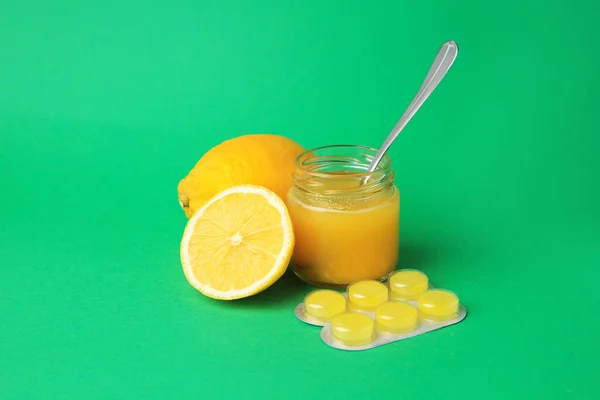 Blister with cough drops, fresh lemons and honey on green background