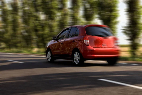 Red car driving at high speed on asphalt road outdoors, motion blur effect
