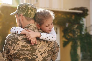 Soldier in Ukrainian military uniform hugging his daughter outdoors, space for text. Family reunion