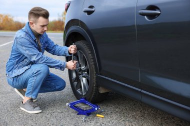 Young man changing tire of car on roadside