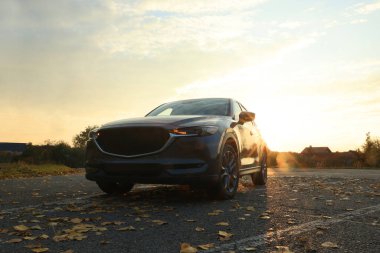 Siyah modern araba gün batımında yola park edilmiş.