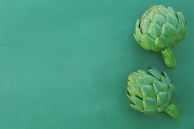 Whole fresh raw artichokes on green background, flat lay. Space for text