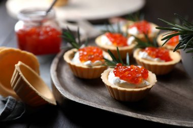 Delicious tartlets with red caviar and cream cheese served on wooden table, closeup