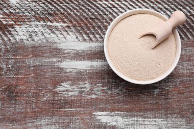 Bowl and scoop with active dry yeast on wooden table, top view. Space for text