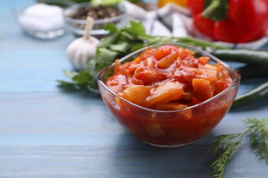 Bowl of delicious lecho on light blue wooden table, closeup. Space for text