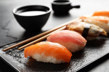 Serving board with delicious nigiri sushi and soy sauce on black table, closeup