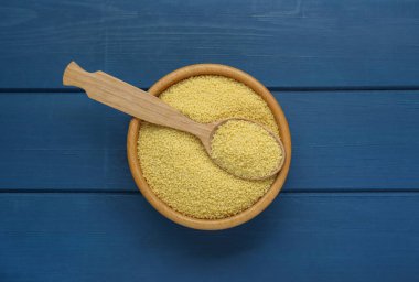 Bowl and spoon with raw couscous on blue wooden table, top view
