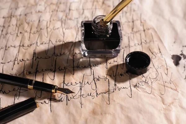 Open inkwell and fountain pens on vintage parchment with text, closeup