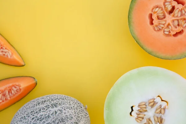 Different tasty ripe melons on yellow background, flat lay. Space for text