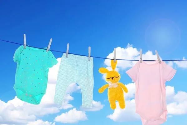 Baby clothes and crochet toy drying on washing line against sky