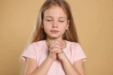 Bej arka planda dua eden elleri sımsıkı bağlı bir kız