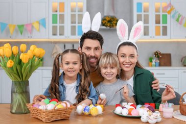 Portrait of happy family with Easter eggs at table in kitchen
