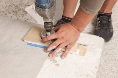 Worker with electric drill preparing tiles for installation indoors, closeup