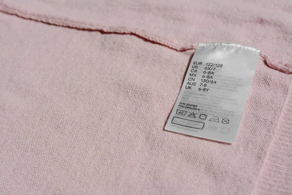 Clothing label with instruction on pink garment, closeup