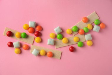 Different tasty chewing gums on pink background, flat lay