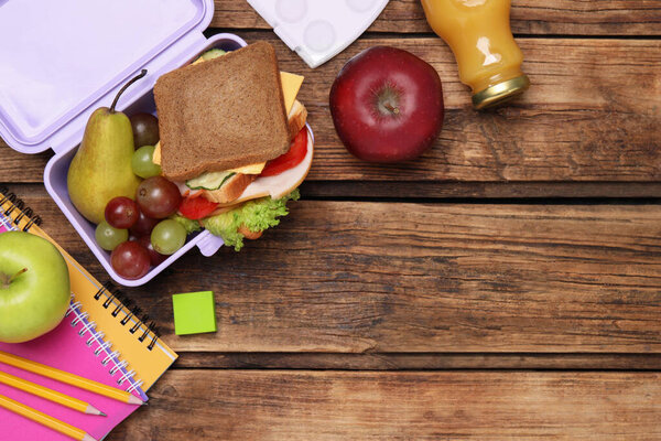 Flat lay composition with lunch box, tasty healthy food and school stationery on wooden table. Space for text