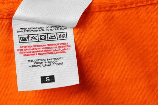 Clothing labels on orange garment, top view. Space for text