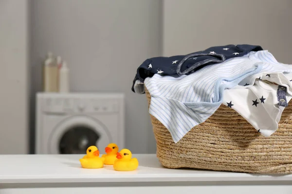 Laundry basket with baby clothes and rubber ducks on table in bathroom, closeup. Space for text