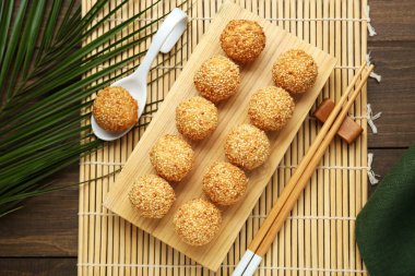 Delicious sesame balls, spoon, green leaves and chopsticks on wooden table, flat lay
