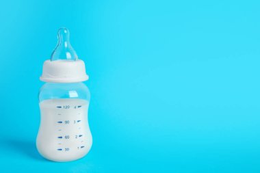 One feeding bottle with milk on light blue background. Space for text