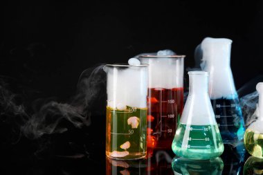 Laboratory glassware with colorful liquids and steam on black background. Chemical reaction